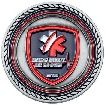 Antiqued silver challenge coin featuring a red and blue shield with a Star of Life and McLean County Area EMS System text.