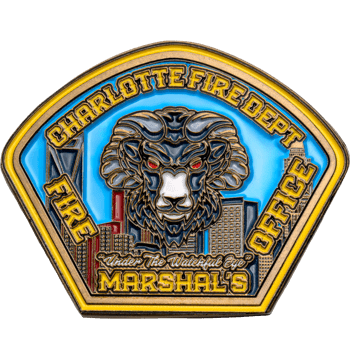 Shield-shaped challenge coin for Charlotte Fire Dept Fire Marshal's Office featuring a horned ram head with red eyes over a city skyline background.