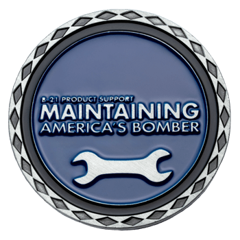 Circular challenge coin with blue enamel, silver wrench icon, and text 'Maintaining America's Bomber' with a diamond pattern border.