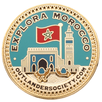 Gold pin with Explora Morocco text, featuring the Moroccan flag, a mosque minaret, camels, and a decorative gold border.